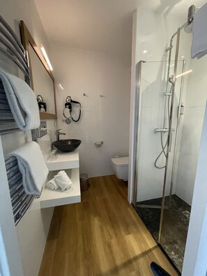 Un baño moderno con suelo de madera, cabina de ducha de vidrio, lavabo blanco y un inodoro.