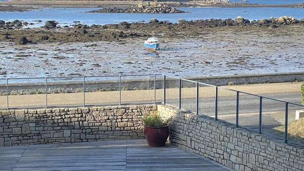 Vista costera con playa rocosa, un bote y un muro de piedra con una maceta.