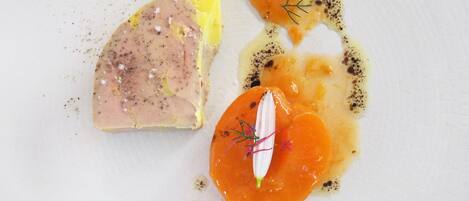 Un plato blanco con un trozo de carne, una porción de comida amarilla y un elemento naranja redondo con una guarnición.
