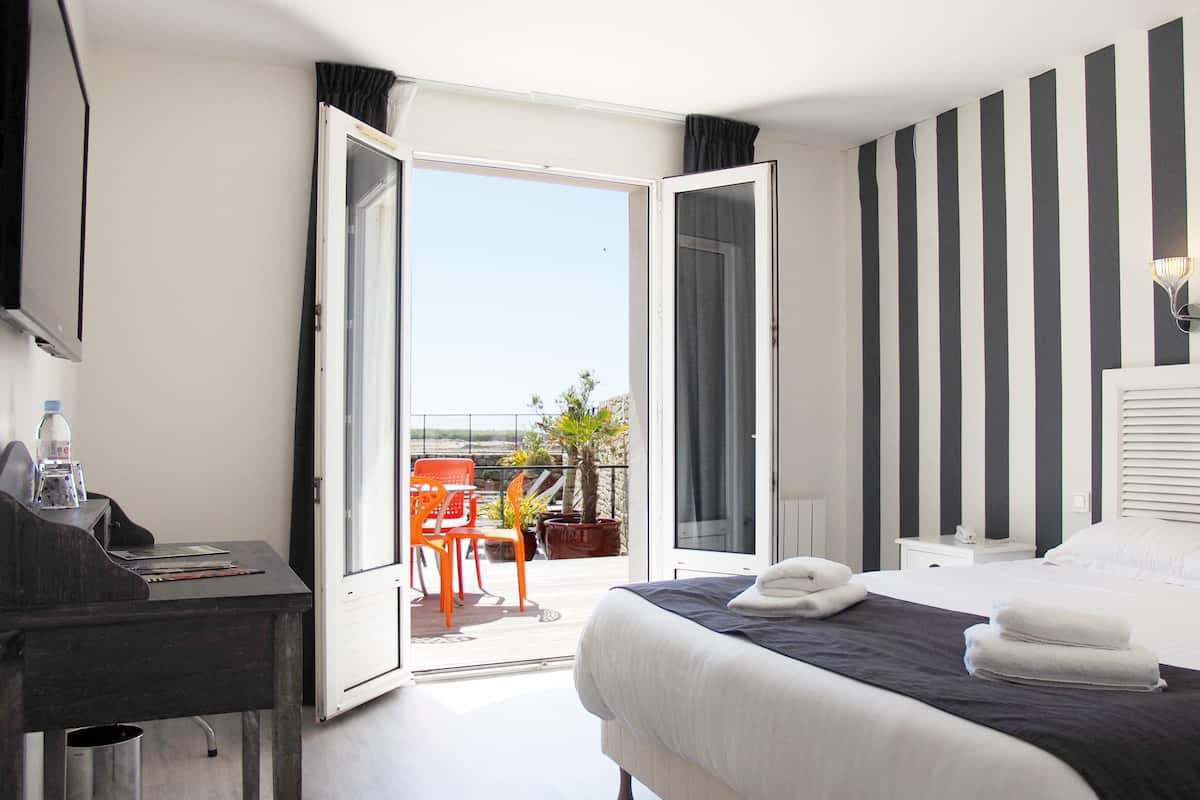 Habitación de hotel con cama, escritorio, silla y balcón con vistas.
