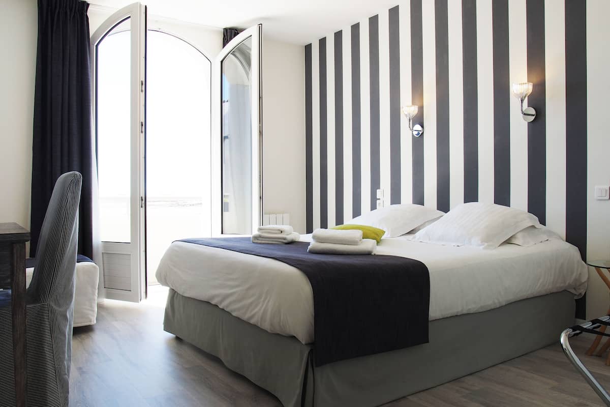 Una habitación de hotel con cama, una silla, una mesita de noche y una ventana con cortinas.