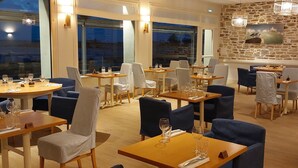 Un restaurante con mesas redondas, sillas azules y blancas, y una pared de piedra con un cuadro.