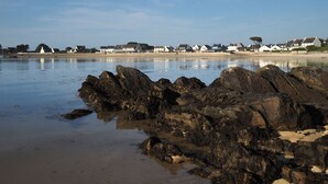 Escena costera con costa rocosa, agua tranquila y una hilera de casas blancas con techos grises.