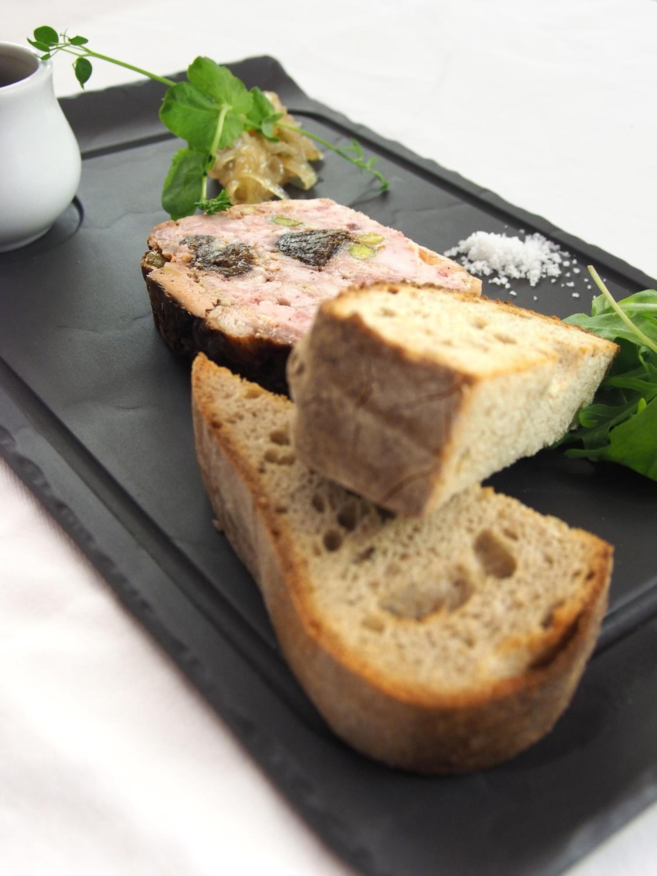 A black slate serving board with a slice of meatloaf, a piece of bread, and some greens.