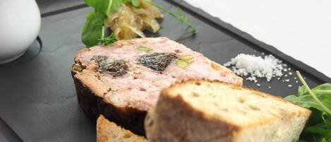 A black slate serving board with a slice of meatloaf, a piece of bread, and some greens.