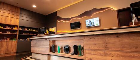 Un área de recepción moderna con paneles de madera, una barra con varios artículos y un televisor montado.