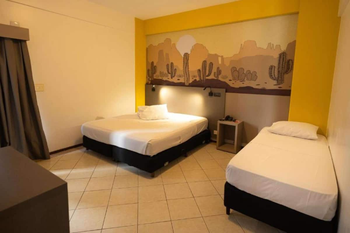 A hotel room with two beds, a desk, and a mural of cacti on the wall.