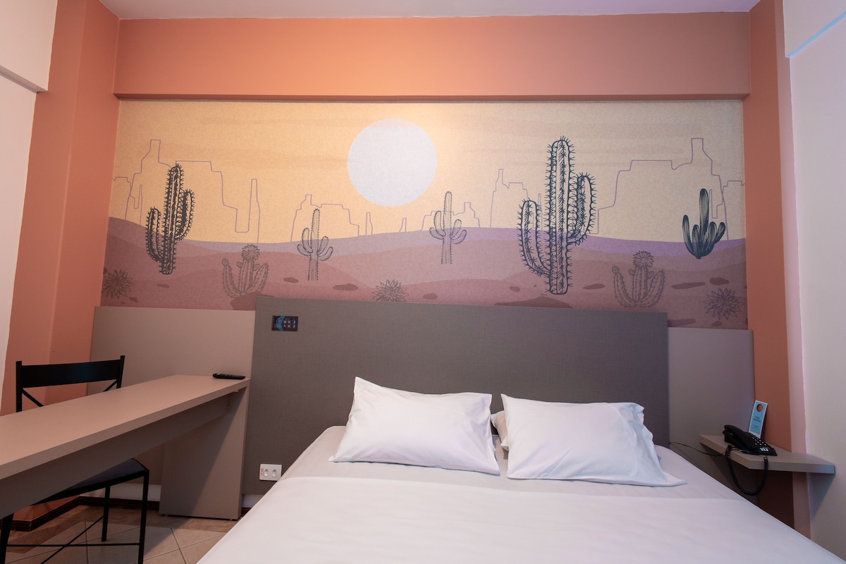 A hotel room with a bed, a desk, and a wall mural of a desert scene.