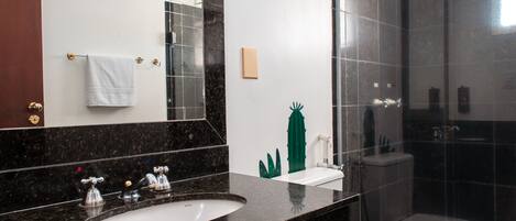 Un baño moderno con lavamanos de mármol negro, inodoro blanco y ducha con mampara de vidrio.