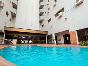 A swimming pool with lounge chairs and tables, surrounded by a multi-story building with balconies and air conditioning units. - ibis Styles Presidente Prudente Portal D'Oeste (Presidente Prudente)