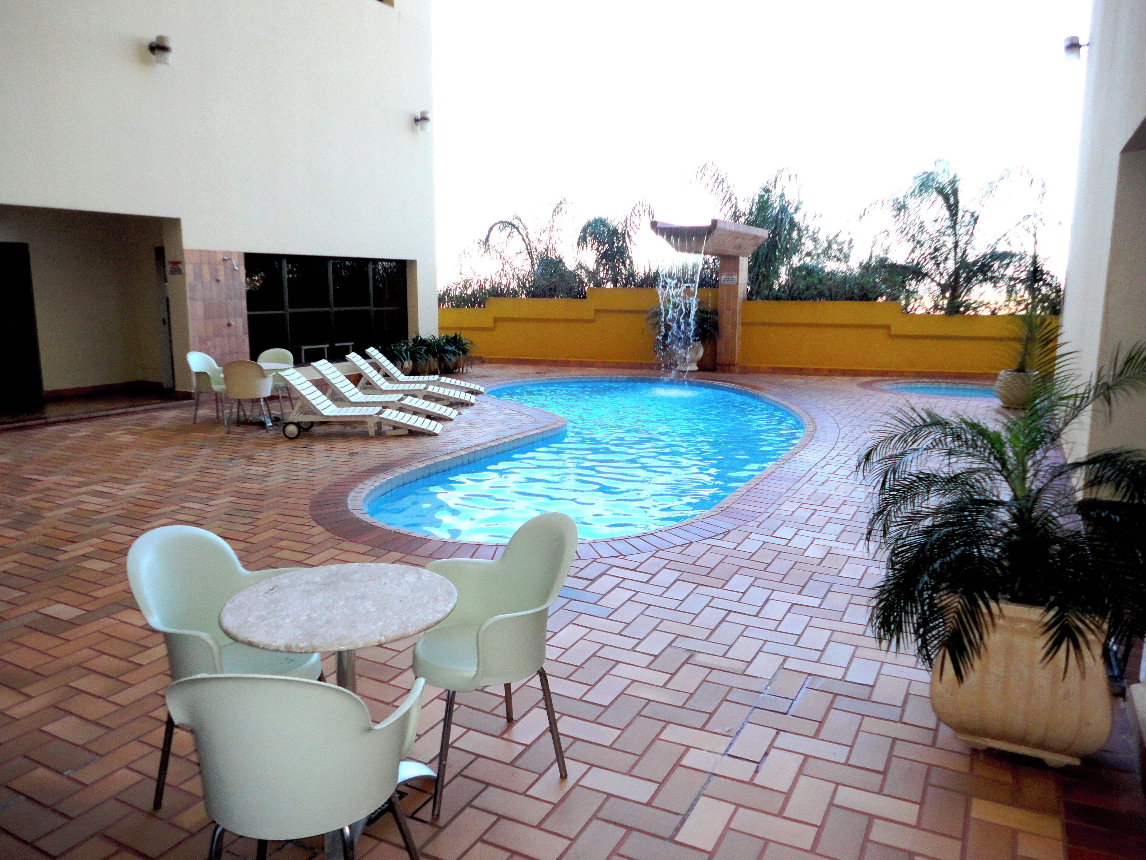 A swimming pool with lounge chairs and tables, surrounded by a tiled patio.