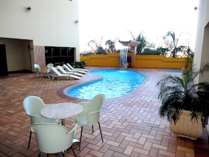 A swimming pool with lounge chairs and tables, surrounded by a tiled patio. - ibis Styles Presidente Prudente Portal D'Oeste (Presidente Prudente)