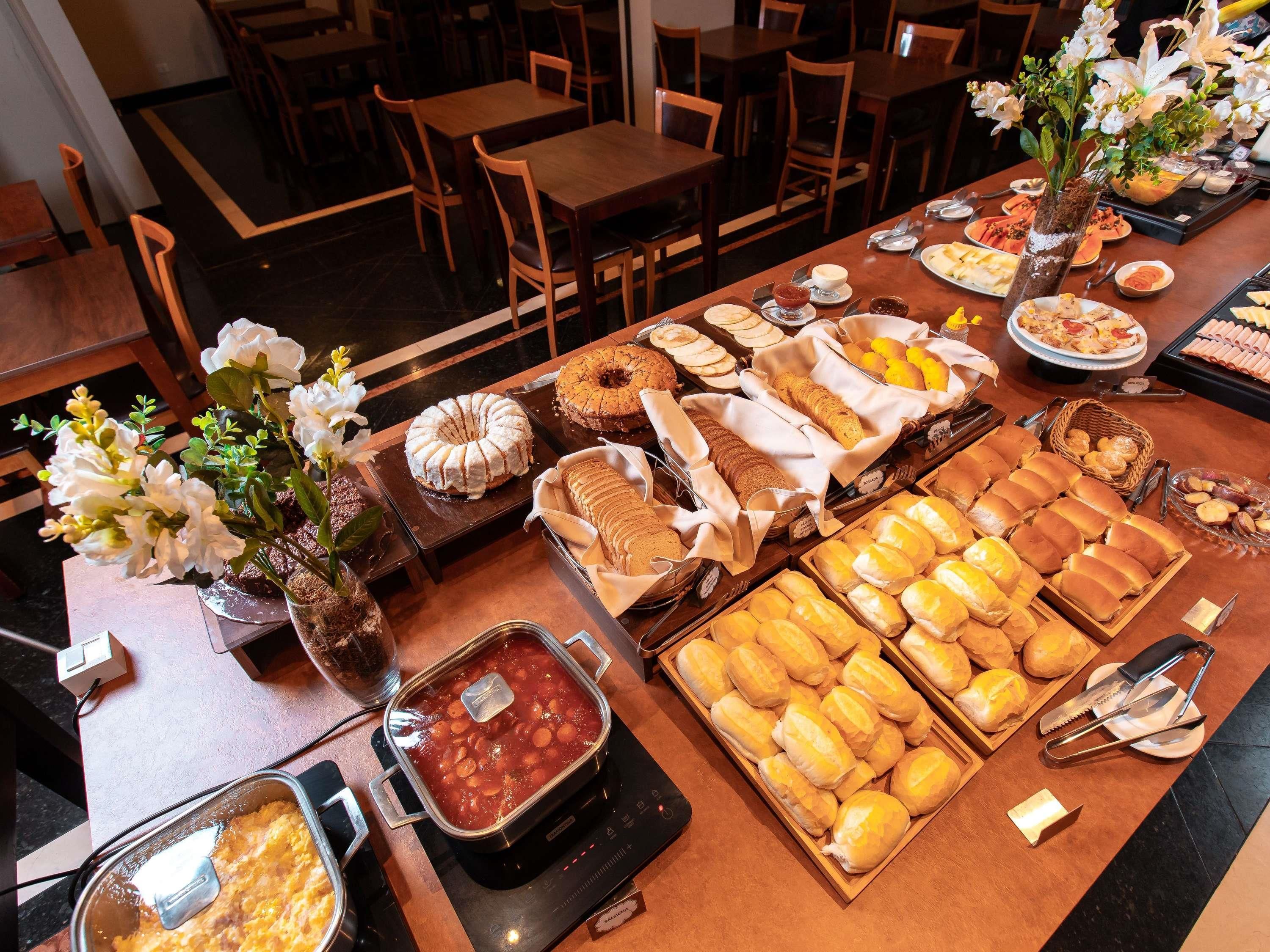 A buffet with various food items, including cakes, pastries, and bread, arranged on a table in a dining area with chairs and tables.