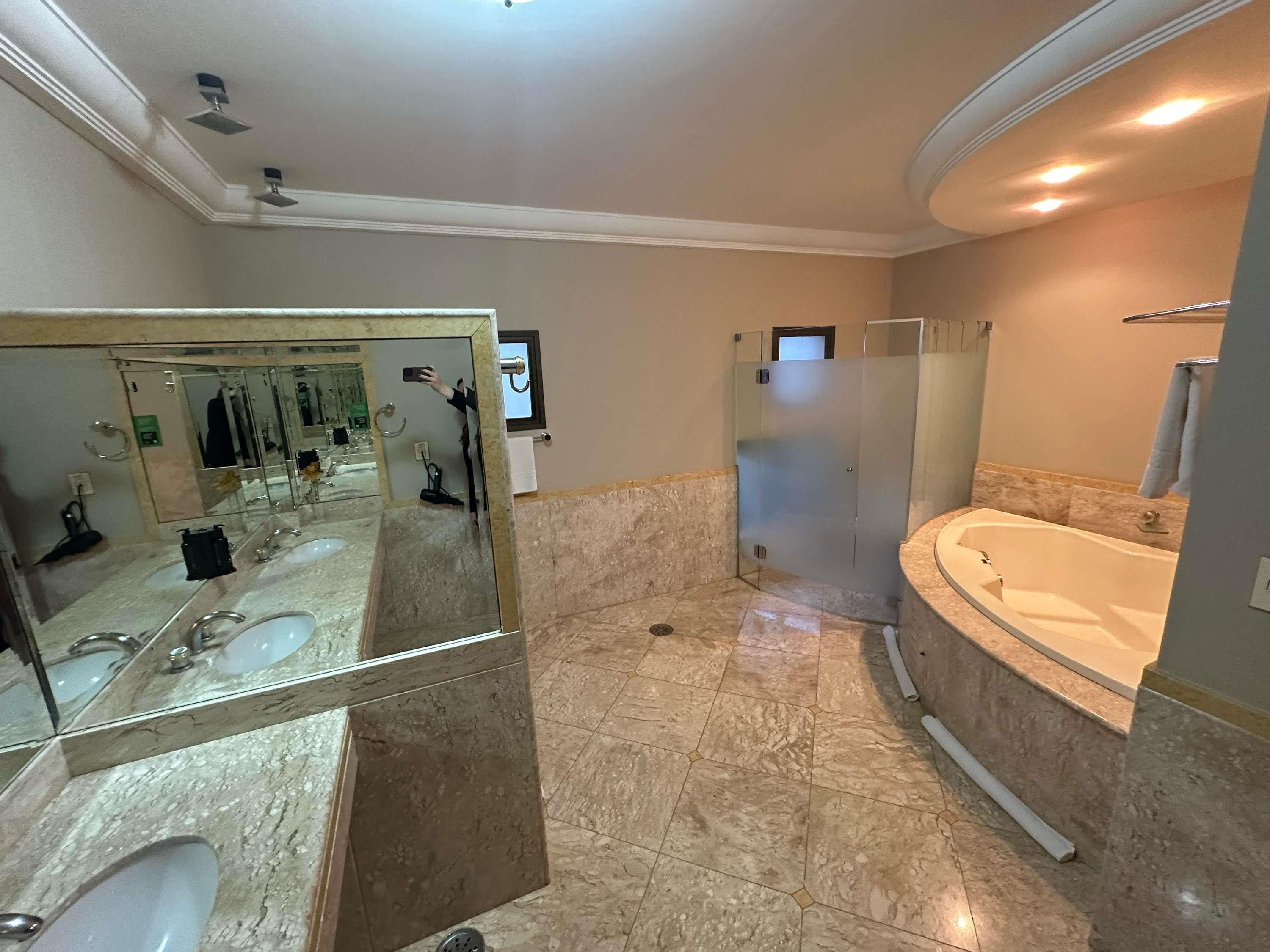 A bathroom with a large mirror, two sinks, a shower enclosure, and a bathtub.