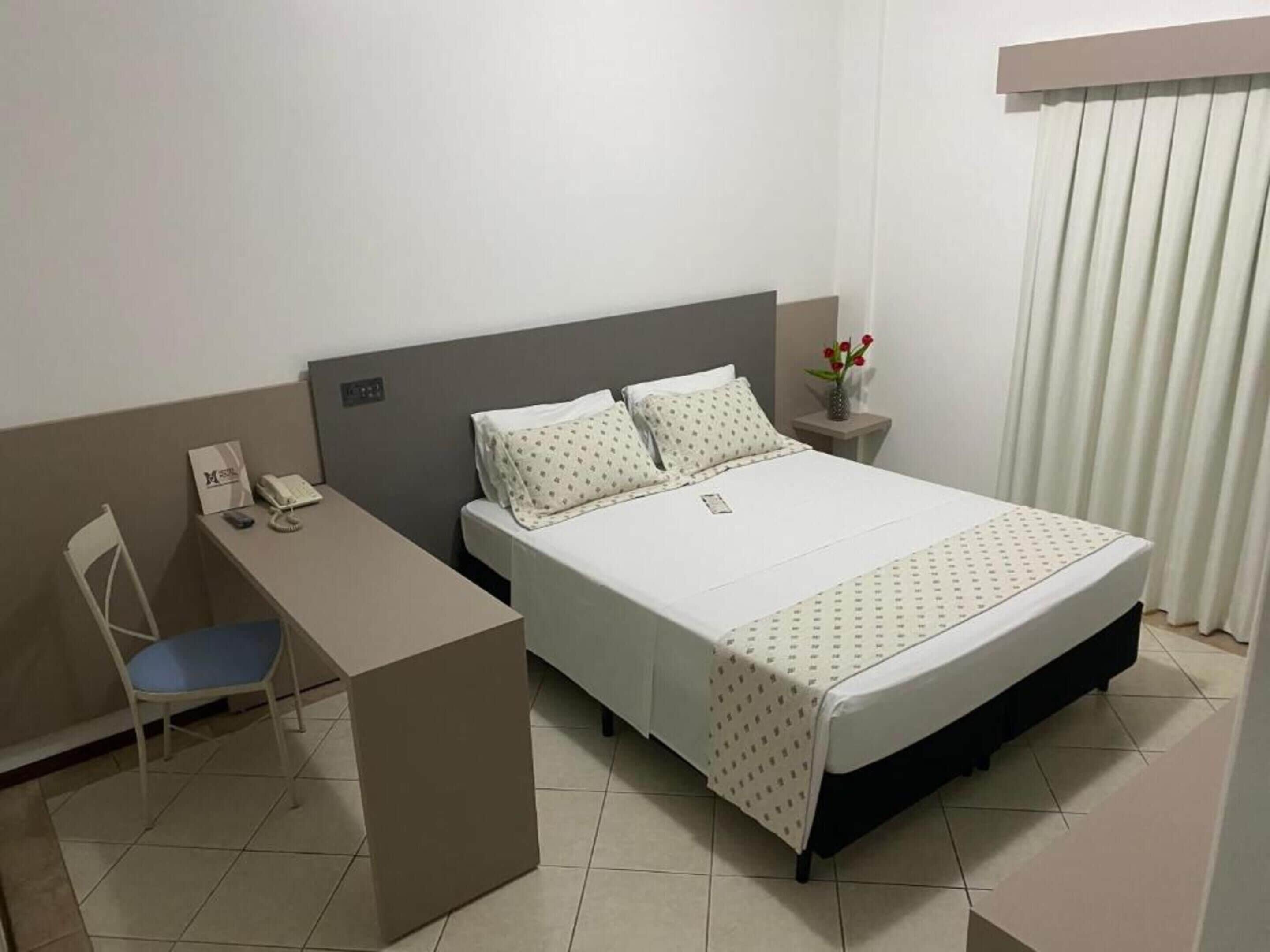 A hotel room with a bed, a desk, and a chair.