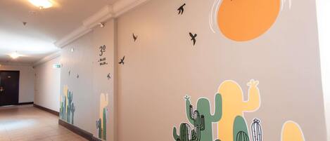 Un pasillo con un mural que muestra cactus y pájaros, una lámpara en el techo y una puerta al final.