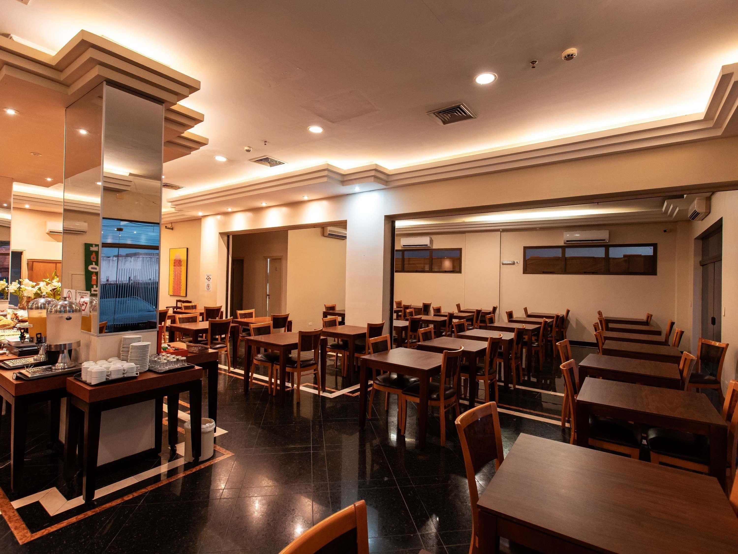 A restaurant with multiple tables and chairs, a buffet area with food and drinks, and a large window with a view.