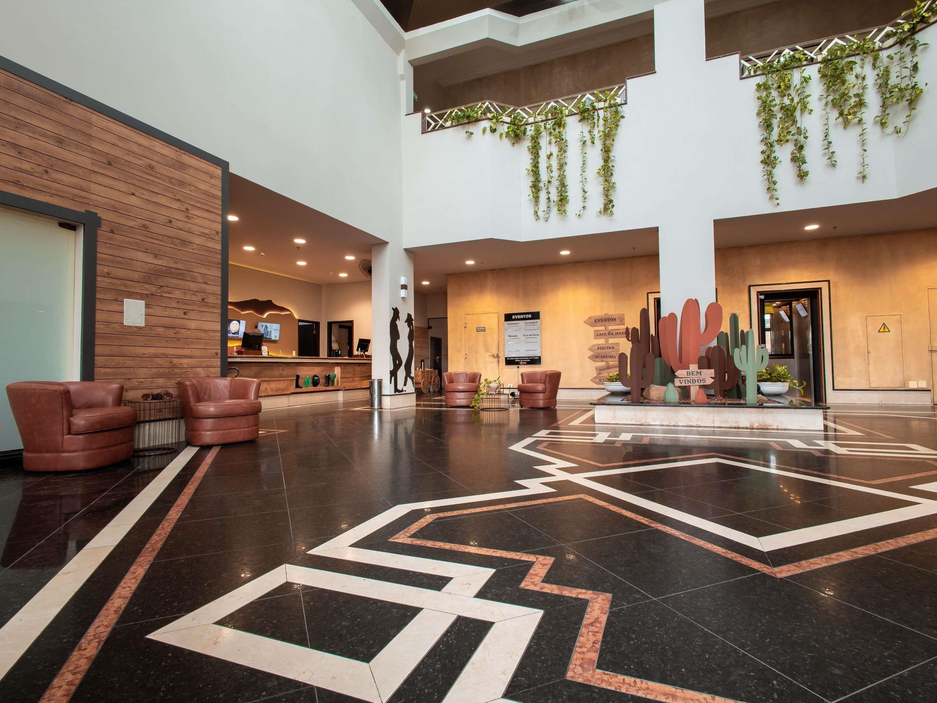 Um hall de entrada com balcão de recepção, poltronas de couro, design geométrico no chão e plantas penduradas.