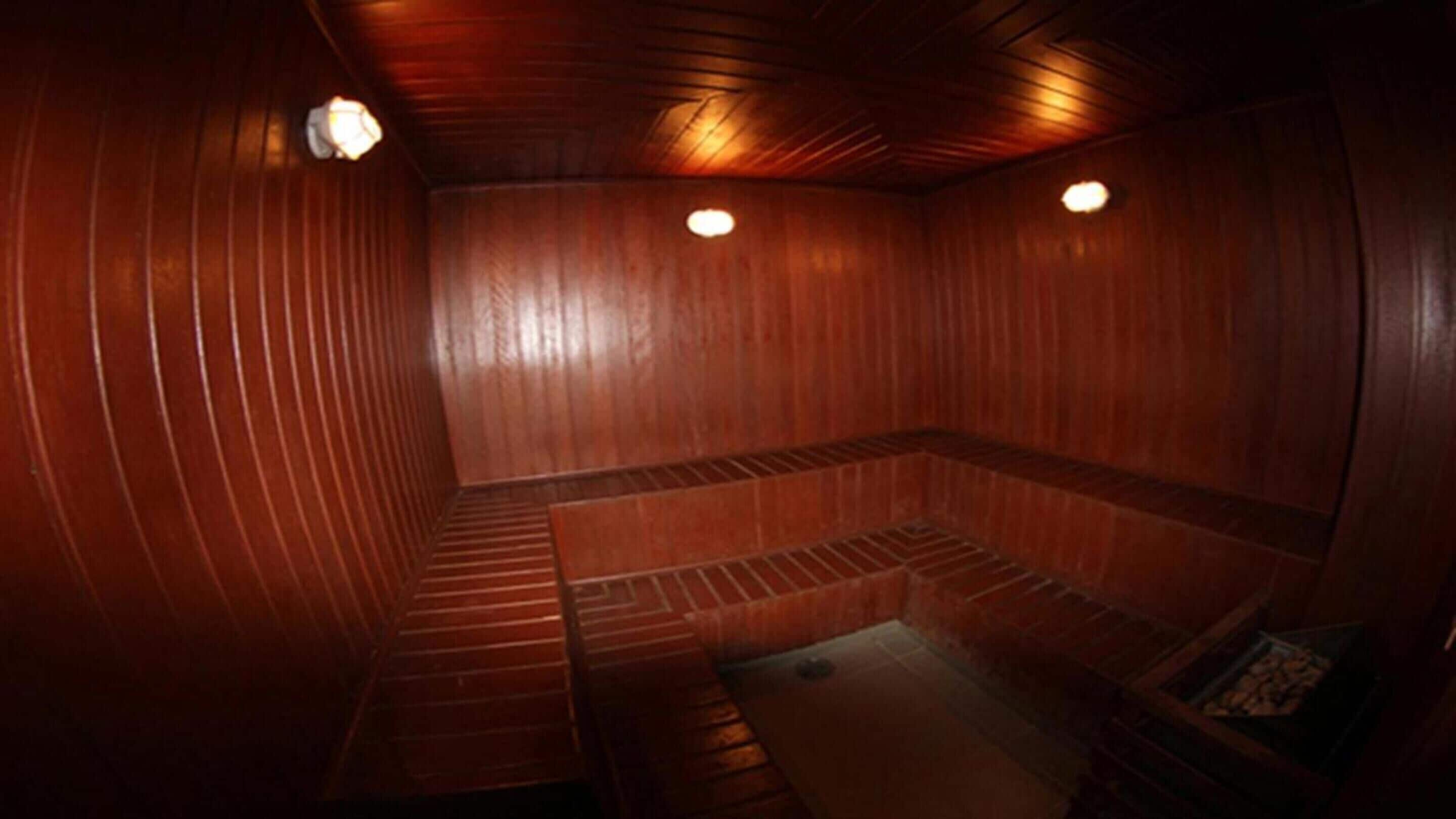 Una sauna con paredes y bancos de madera, un banco en el centro, y dos luces en el techo.