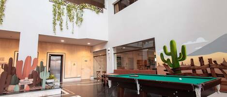 A spacious indoor area with a pool table, a cactus decoration, and a desert mural.