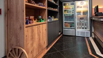 A hotel lobby with wooden shelving, a vintage wooden cart, and a minibar with beverages and snacks.