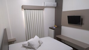 Una habitació d'hotel amb un llit, un petit escriptori, una televisió, aire condicionat i una finestra amb persianes.