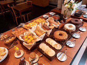 A buffet table with various baked goods, including bread, rolls, and pastries, and a cake on a stand.
