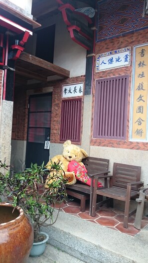 A building entrance with a wooden bench, a large teddy bear, and a potted plant. - Pearl B&B (Jinsha)