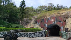 A paved area with a large circular emblem, a stone wall with a camouflage pattern, and a tunnel entrance. - Pearl B&B (Jinsha)