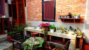 An outdoor seating area with a table covered in a camouflage tablecloth, surrounded by potted plants and a brick wall. - Pearl B&B (Jinsha)