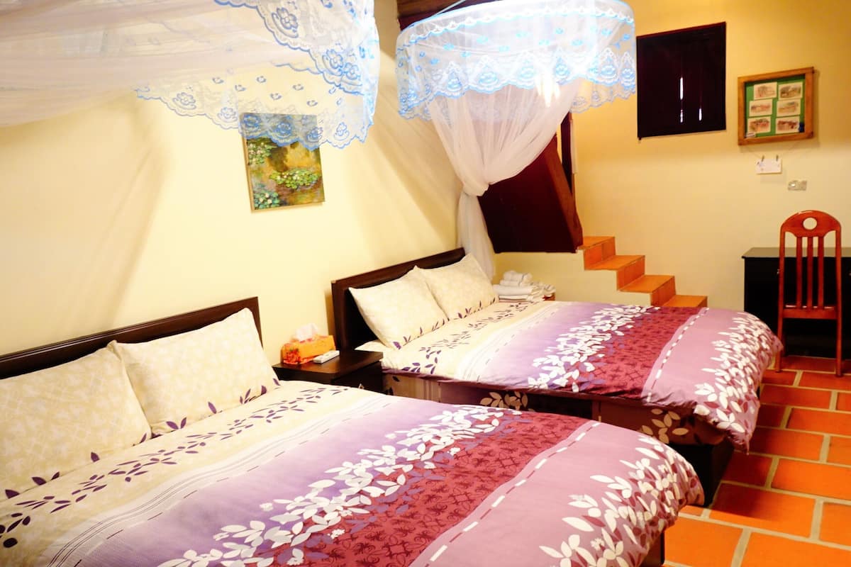 A hotel room with two beds, a wooden desk, a chair, a staircase, and a wall-mounted TV.