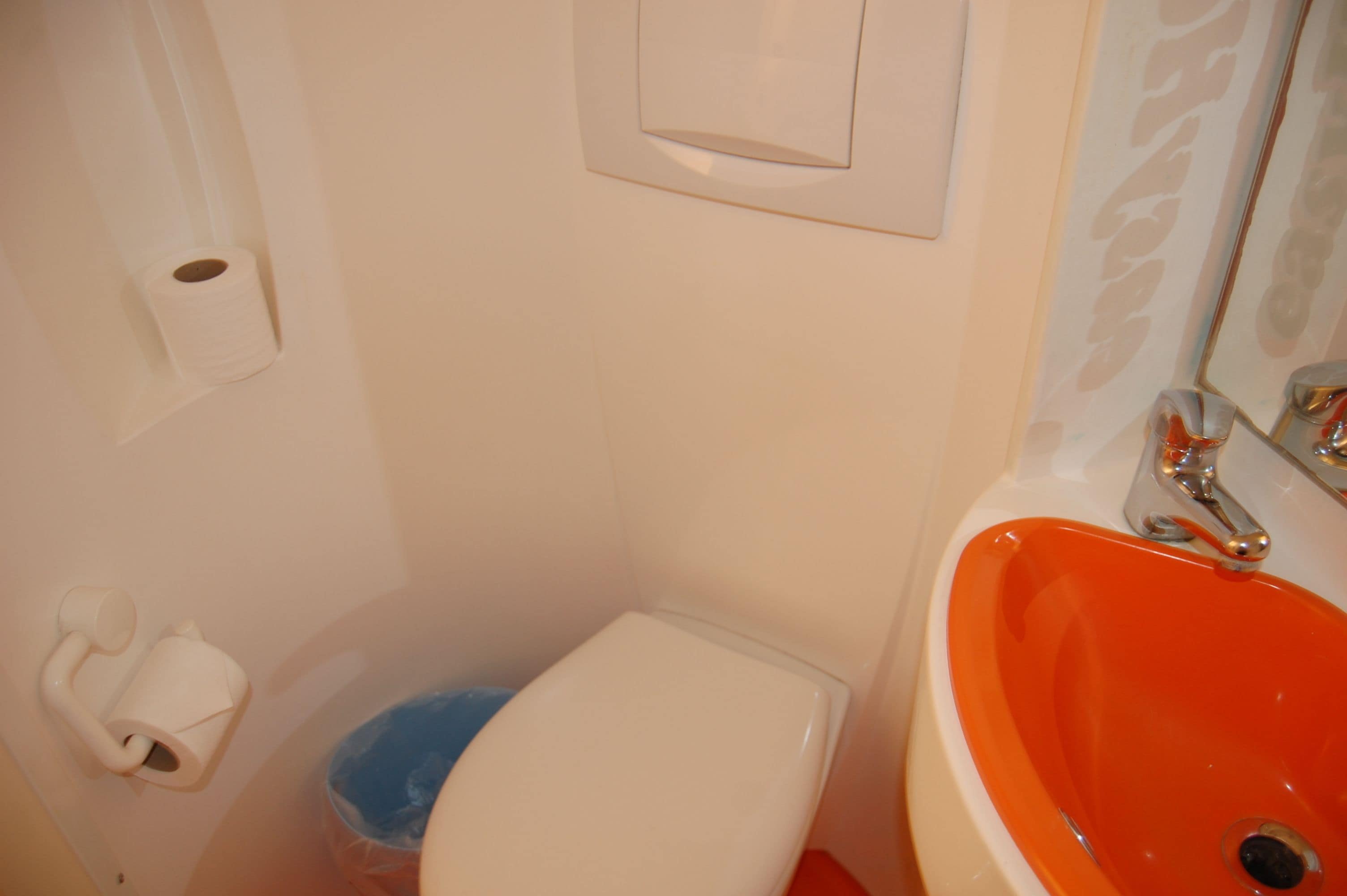 Un baño con un inodoro blanco, un lavabo naranja y un cubo de basura azul.