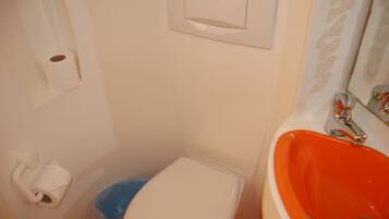 Un baño con un inodoro blanco, un lavabo naranja y un cubo de basura azul.