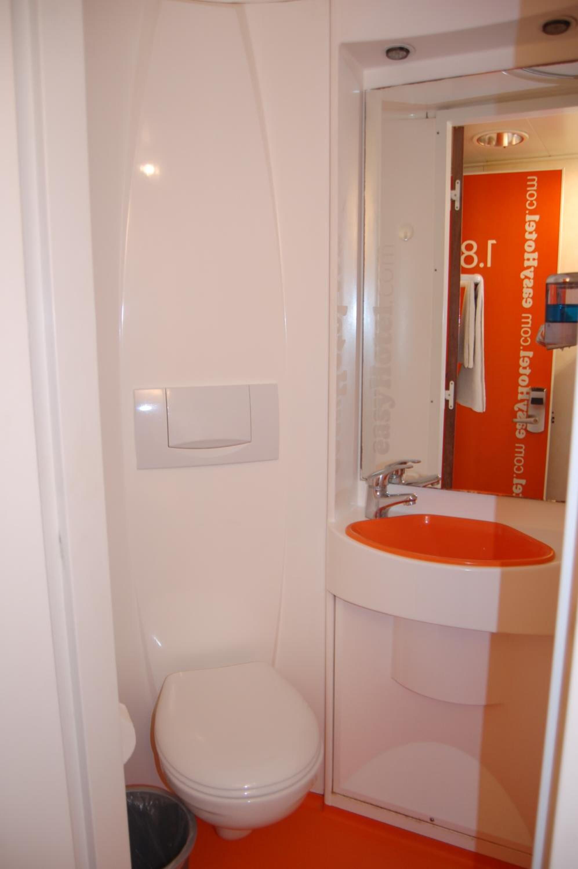 A bathroom with a white toilet, an orange sink, and a glass shower enclosure.