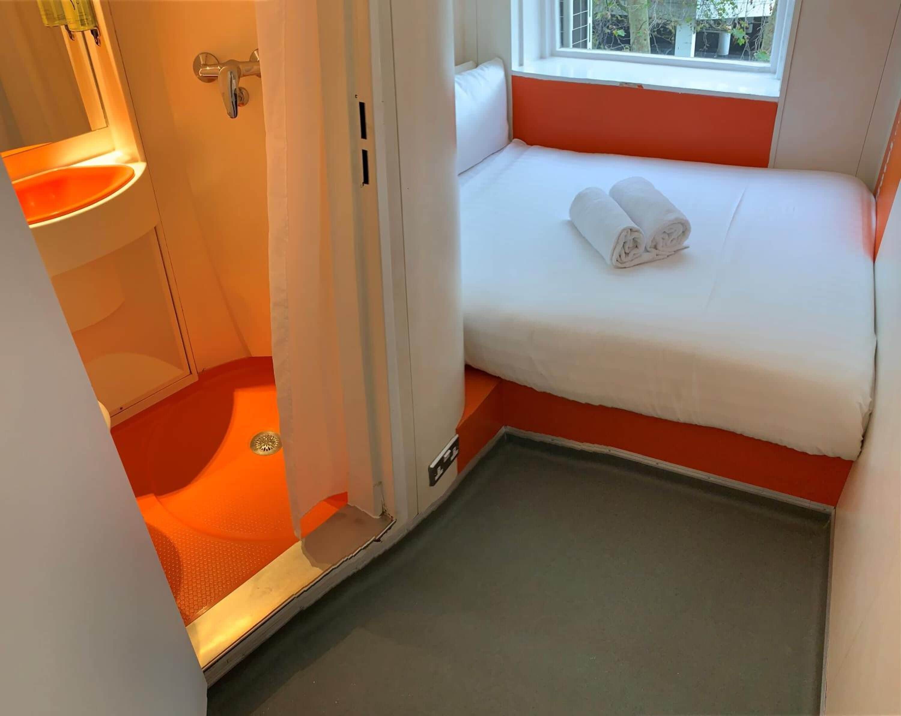 A compact room with a bed, a small window, and a bathroom area.