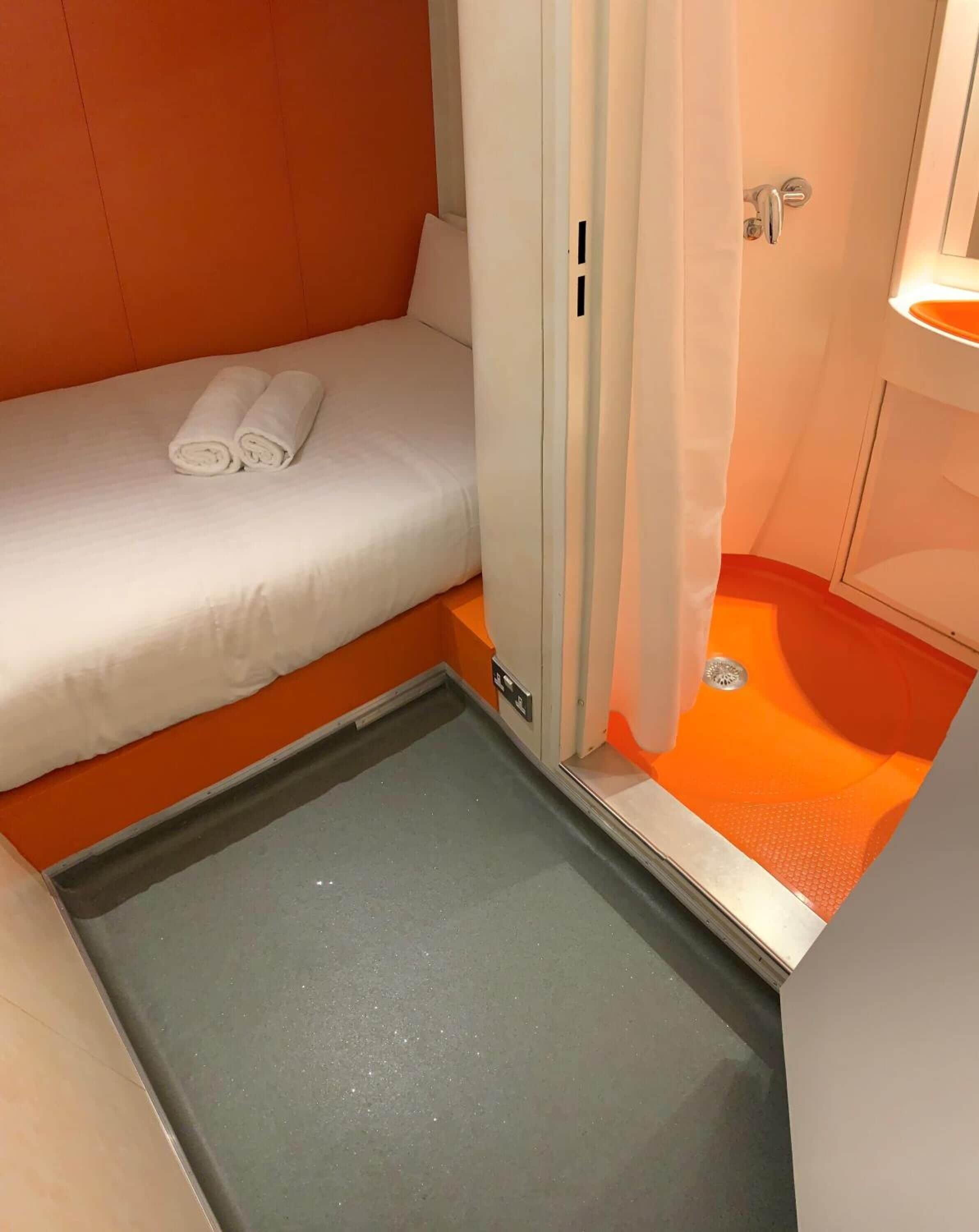 A compact room with a bed, a small bathroom, and a shower area.