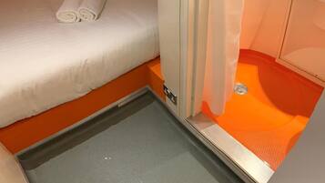 A compact room with a bed, a small bathroom, and a shower area.