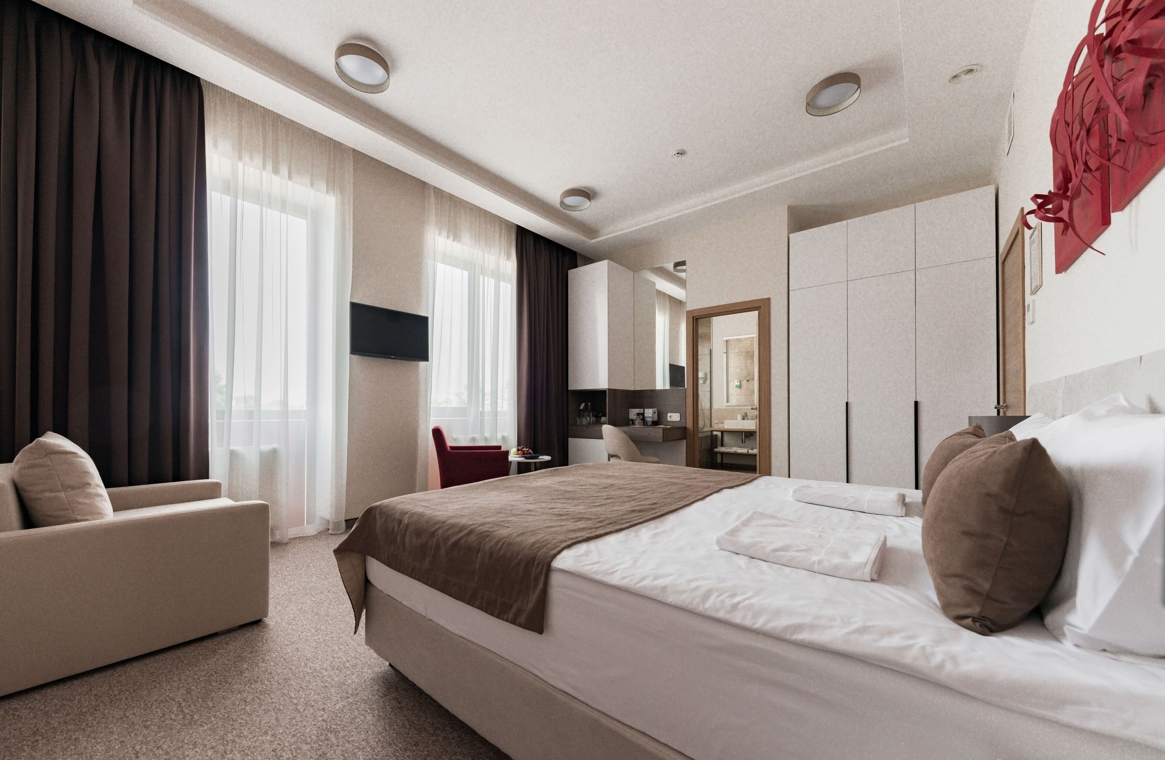 A modern hotel room with a large bed, a sofa, a desk, and a mirror.