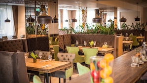 A restaurant with wooden tables and green upholstered chairs, featuring hanging pendant lights and potted plants. - Wish Aqua & Spa Resort (Vyshen'ky)