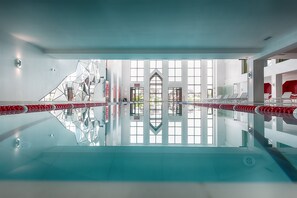 A modern indoor swimming pool with clear glass walls, a geometric ceiling design, and a view of a building outside. - Wish Aqua & Spa Resort (Vyshen'ky)