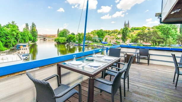Una terraza con una mesa y sillas que da a un río, con barcos amarrados cerca.