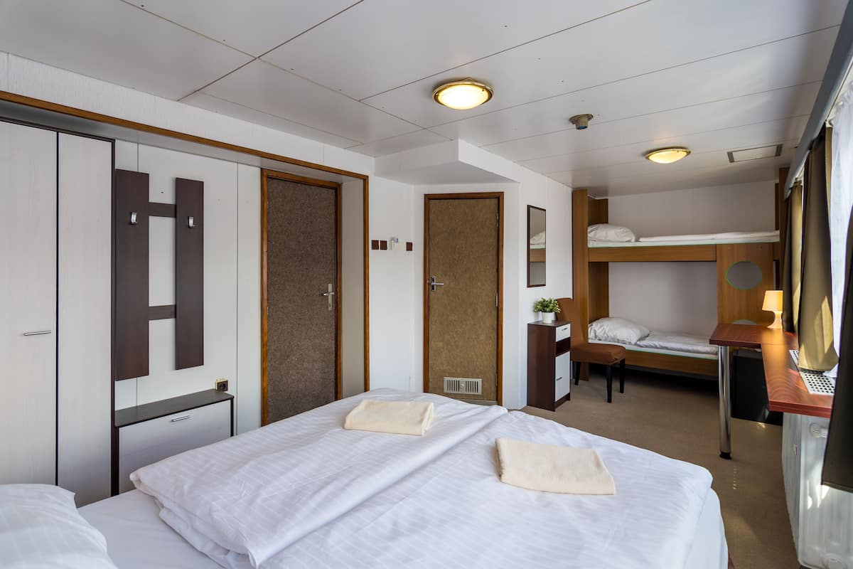 Habitación de hotel con una cama grande, una cama más pequeña, un escritorio con lámpara, un armario y la puerta del baño.