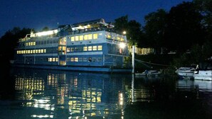 Un barco grande de varios pisos con múltiples cubiertas, atracado en un puerto deportivo por la noche.