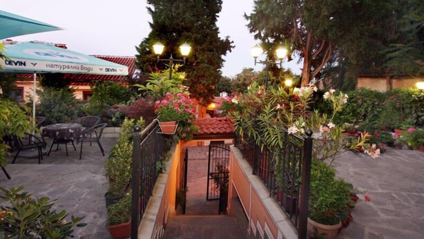 An outdoor patio area with a covered seating area, potted plants, and a staircase leading to a building entrance. - Alafrangite Hotel (Plovdiv)