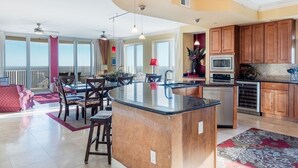 A spacious kitchen with a large island, wooden cabinets, and a dining area with chairs and a table. - Mustique 901 (Gulf Shores)