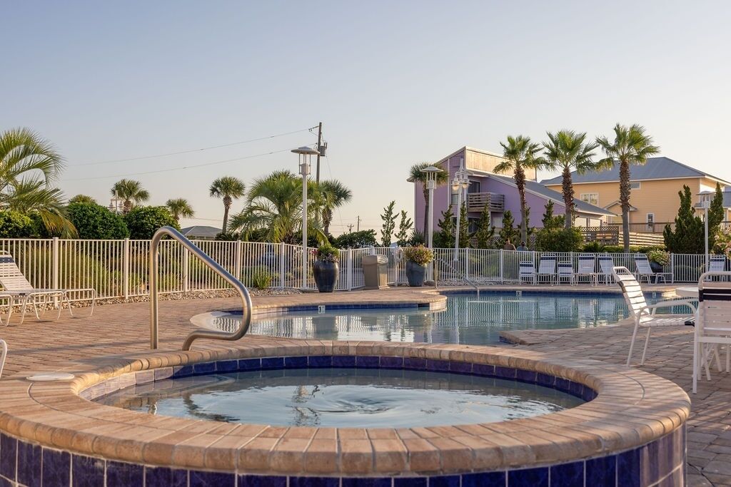 A swimming pool with a hot tub, surrounded by palm trees and lounge chairs.