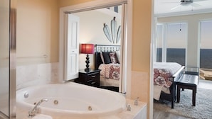 A modern bathroom with a large bathtub, a mirror, and a view of the sea through the adjacent bedroom. - Mustique 901 (Gulf Shores)