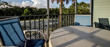 A deck with two chairs, a table, and a view of the beach and palm trees.