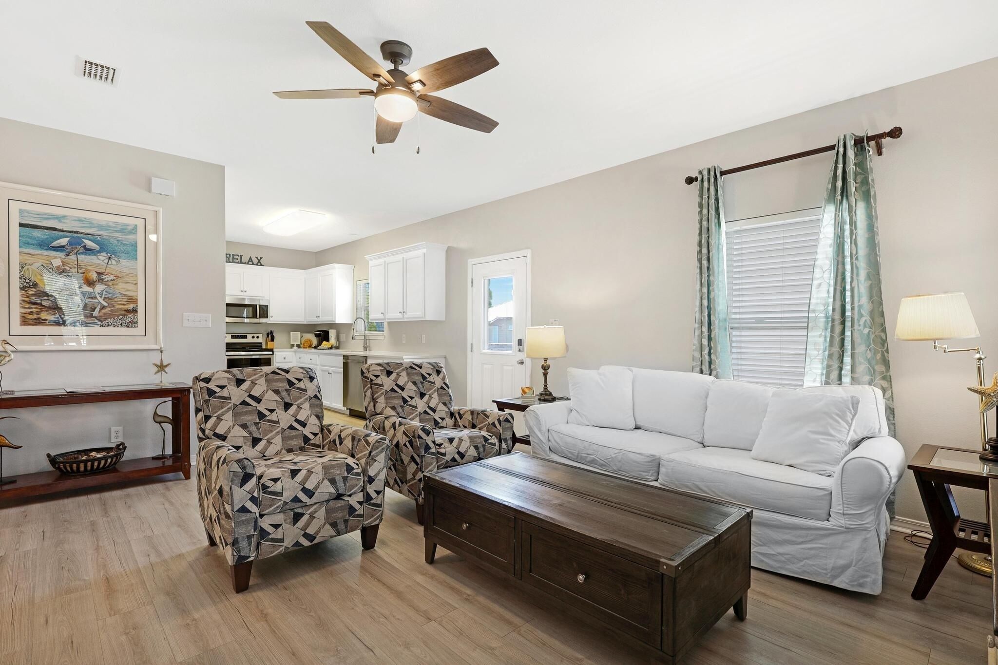 A living room with a white sofa, patterned armchairs, a coffee table, and a ceiling fan.