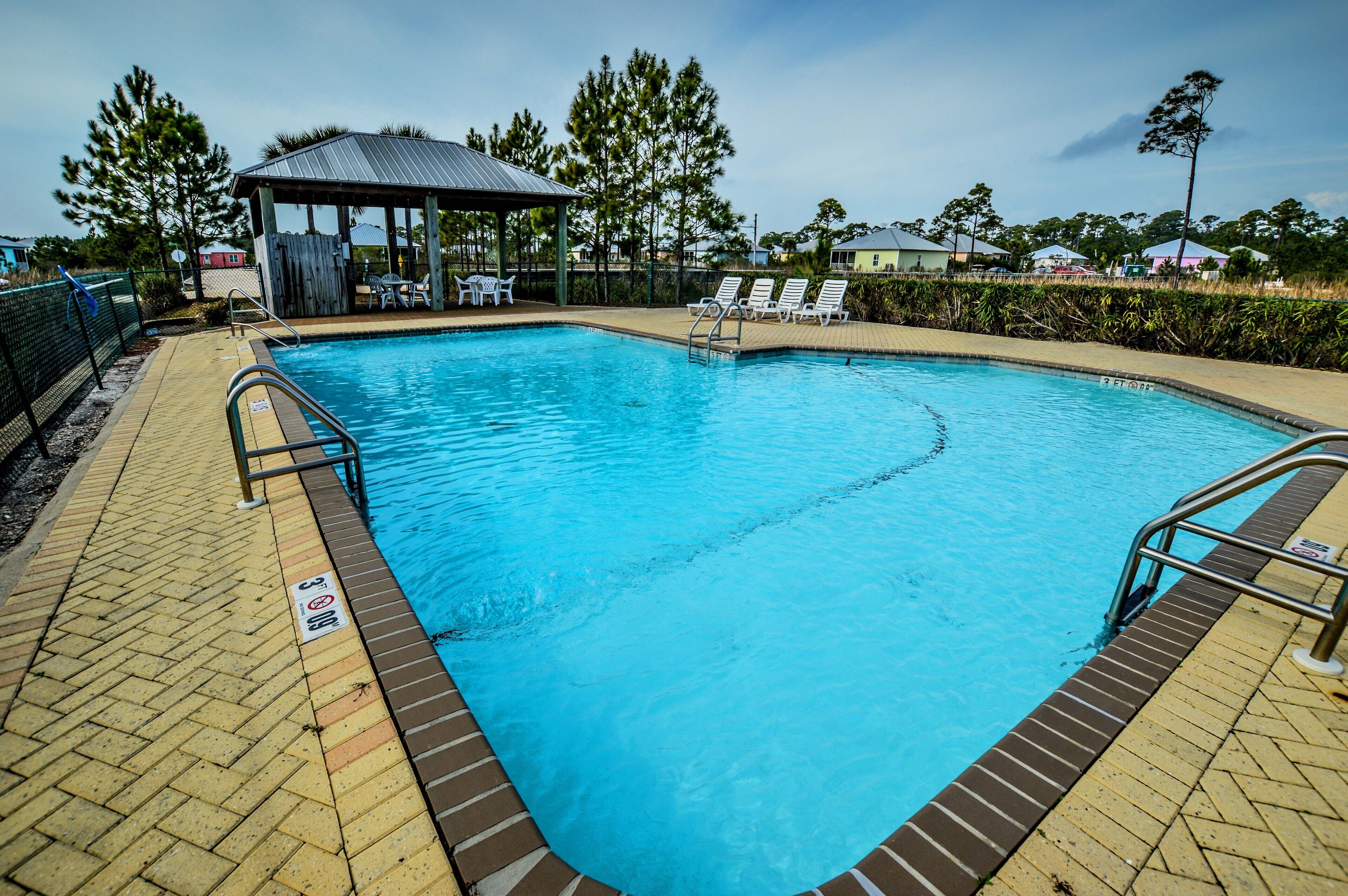 A rectangular swimming pool with a tiled deck, a covered seating area, and lounge chairs.